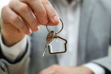 Real estate agent holding house key with trinket, closeup