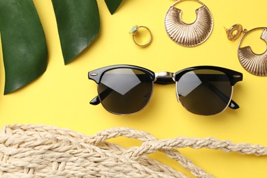 New stylish sunglasses, jewelry and bag on yellow background, flat lay