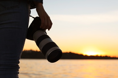 Female photographer with professional camera on riverside at sunset