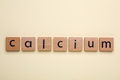 Word Calcium made of wooden cubes with letters on beige background, top view