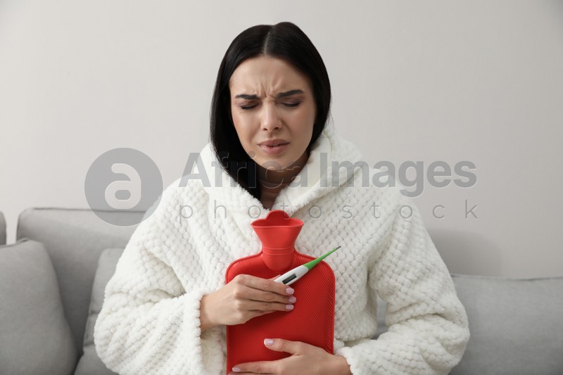 Ill woman with hot water bottle checking her temperature at home