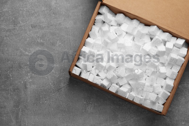 Cardboard box filled with polystyrene styrofoam pieces on grey background, top view. Space for text