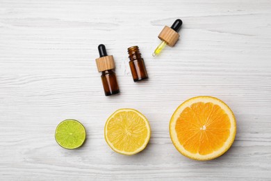 Bottles of citrus essential oils and fresh fruits on white wooden table, flat lay