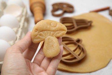 Photo of Woman holding unbaked mushroom shaped cookie at white table, closeup
