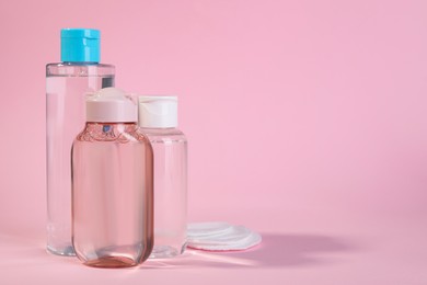 Bottles of micellar water and cotton pads on pink background. Space for text