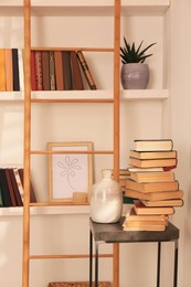 Stack of different books and vase on table near bookshelves in home library