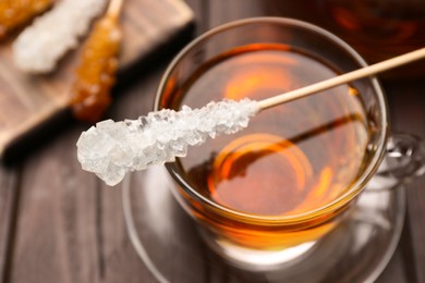 Stick with sugar crystals and cup of tea on wooden table, closeup