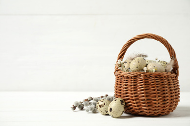 Quail eggs and flowers in wicker basket on white wooden table, space for text. Easter celebration