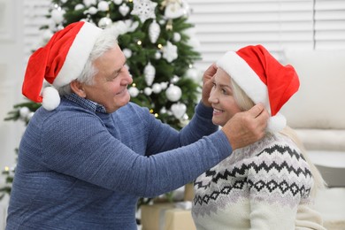 Happy mature couple in Santa hats at home. Christmas celebration
