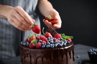 Woman decorating delicious chocolate cake with fresh strawberries at table, closeup