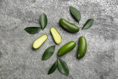 Fresh seedless avocados with green leaves on grey table, flat lay