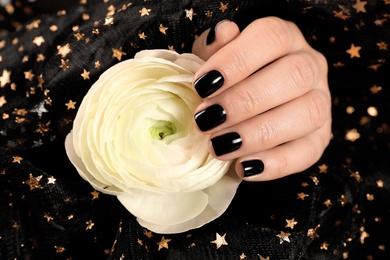 Woman with black manicure holding beautiful flower on dark background, closeup. Nail polish trends