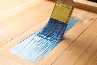 Applying blue paint onto wooden surface, closeup