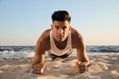 Sporty man doing plank on sandy beach