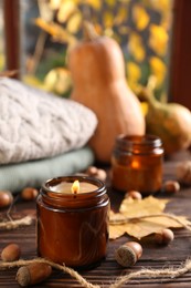 Burning scented candles, warm sweaters and acorns on wooden table near window. Autumn coziness