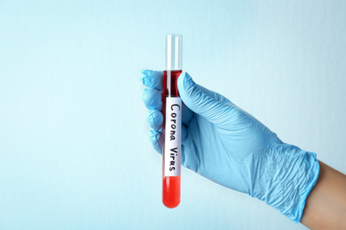 Woman holding test tube with red liquid and inscription CORONA VIRUS on light background, closeup