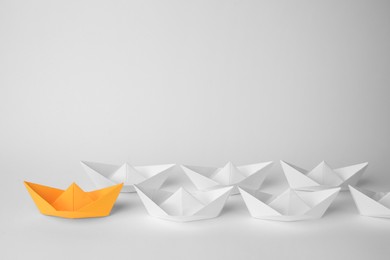 Photo of Group of paper boats following orange one on white background, space for text. Leadership concept