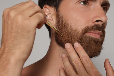 Man applying oil onto beard on grey background, closeup