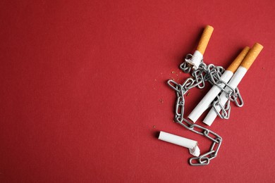 Cigarettes and chain on red background, flat lay with space for text. Quitting smoking concept