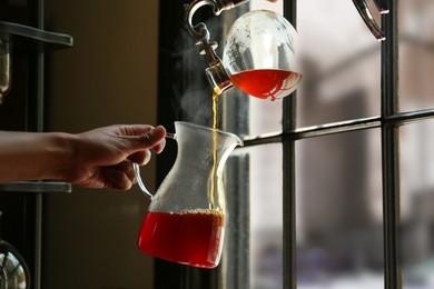Photo of Barista pouring coffee from vacuum maker into glass jug in cafe, closeup. Space for text