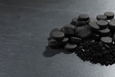 Activated charcoal pills on black table, closeup with space for text. Potent sorbent