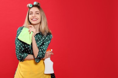 Young housewife with detergent and rag on red background. Space for text
