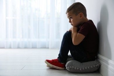 Sad little boy near white wall indoors, space for text. Domestic violence concept
