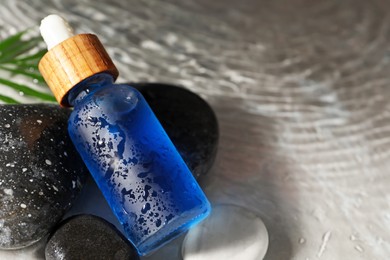 Bottle of face serum and spa stones in water on light background, closeup. Space for text