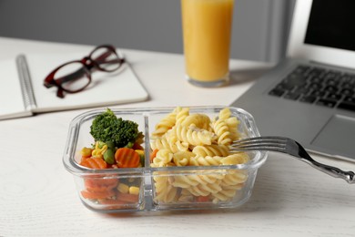Photo of Container with tasty food, laptop, fork and glasses on white wooden table. Business lunch
