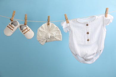 Baby clothes and accessories hanging on washing line against light blue background