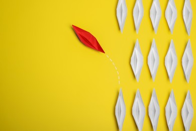Photo of Red paper boat floating away from others on yellow background, flat lay with space for text. Uniqueness concept
