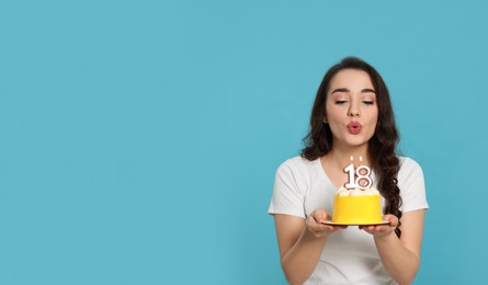 Photo of Coming of age party - 18th birthday. Woman blowing number shaped candles on cake against light blue background, space for text