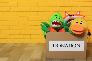 Donation box with different soft toys on floor near yellow brick wall, space for text