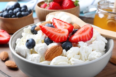 Bowl of fresh cottage cheese, berries and almonds on wooden board, closeup