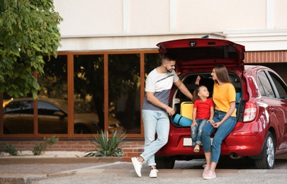 Happy family near car with open trunk on street