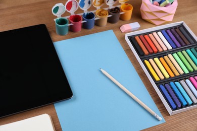 Blank sheet of paper, colorful chalk pastels, tablet and other drawing tools on wooden table. Modern artist's workplace
