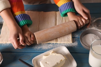 Mother and child rolling dough at blue wooden table together, closeup