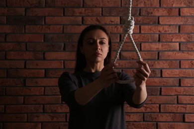 Depressed woman with rope noose near brick wall