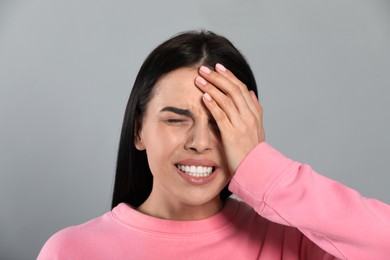 Woman suffering from migraine on grey background