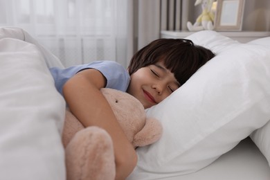 Cute little boy with toy bear sleeping in bed at home
