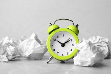 Crumpled paper balls and alarm clock on grey table