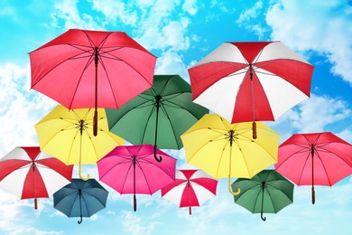 Group of different colorful umbrellas against blue sky with white clouds on sunny day