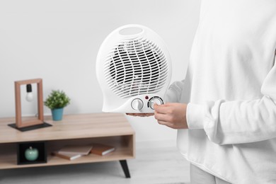 Photo of Woman turning on electric fan heater at home, closeup. Space for text