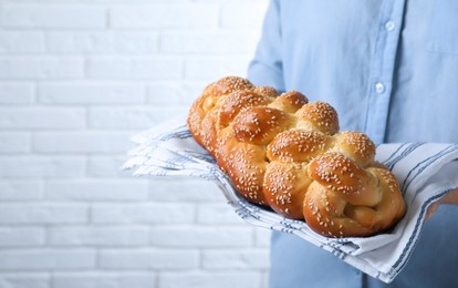 Closeup view of woman holding homemade braided bread near white brick wall, space for text. Traditional Shabbat challah