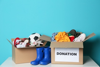 Donation boxes with clothes, shoes and toys on table against color background
