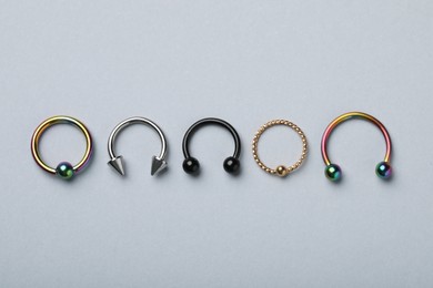 Photo of Stylish captive bead and horseshoe rings on light grey background, flat lay. Piercing jewelry