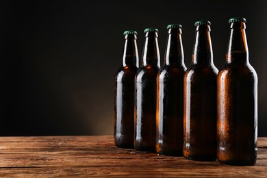 Many bottles of beer on wooden table against dark background, space for text