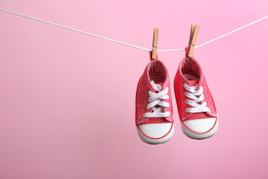 Cute small shoes hanging on washing line against color background, space for text. Baby accessories
