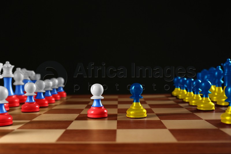 Image of Russian-Ukrainian war, military conflict in 21st century. Chess pieces painted in colors of Ukrainian and Russian flags on wooden board against black background