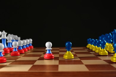 Russian-Ukrainian war, military conflict in 21st century. Chess pieces painted in colors of Ukrainian and Russian flags on wooden board against black background